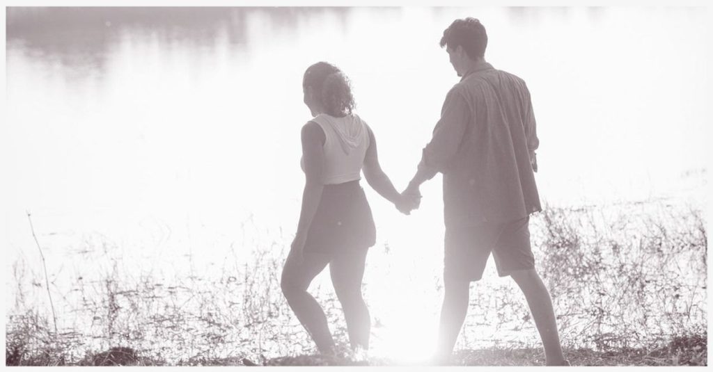 A couple walks alongside a lake while holding hands