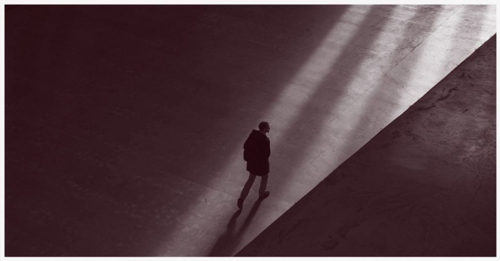 A man walking across a concrete floor towards a source of light