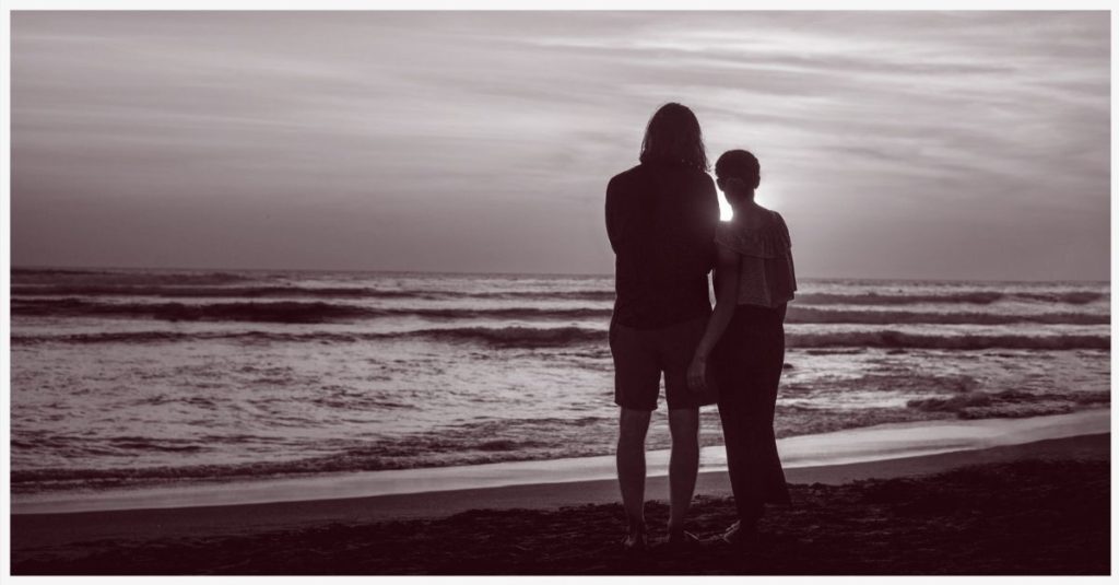 Two people embracing while looking at an ocean sunset