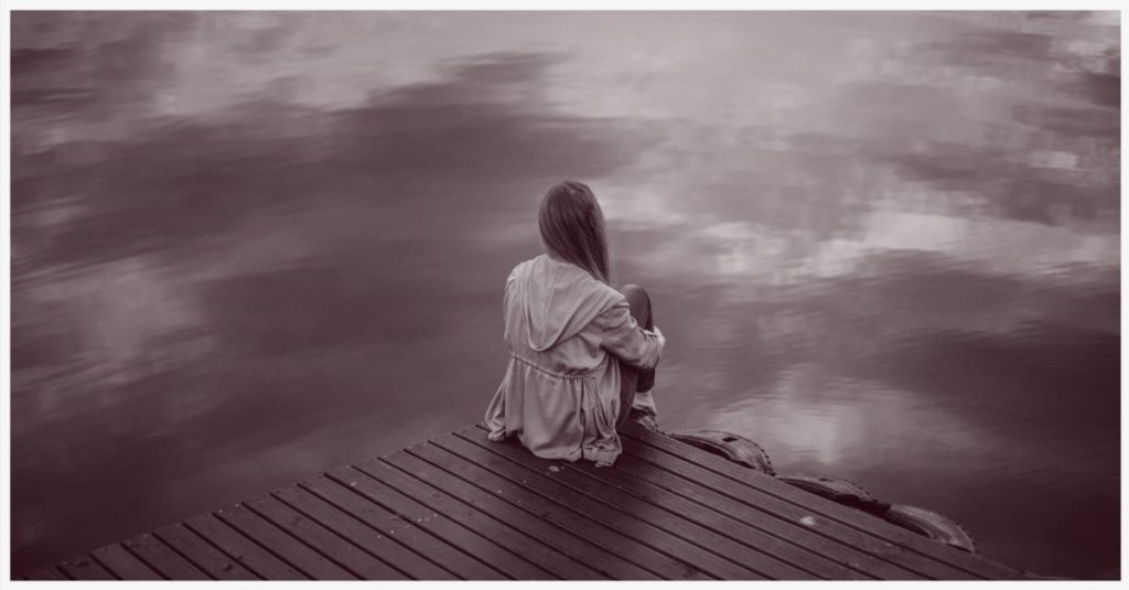 A woman sitting alone on the corner of a dock