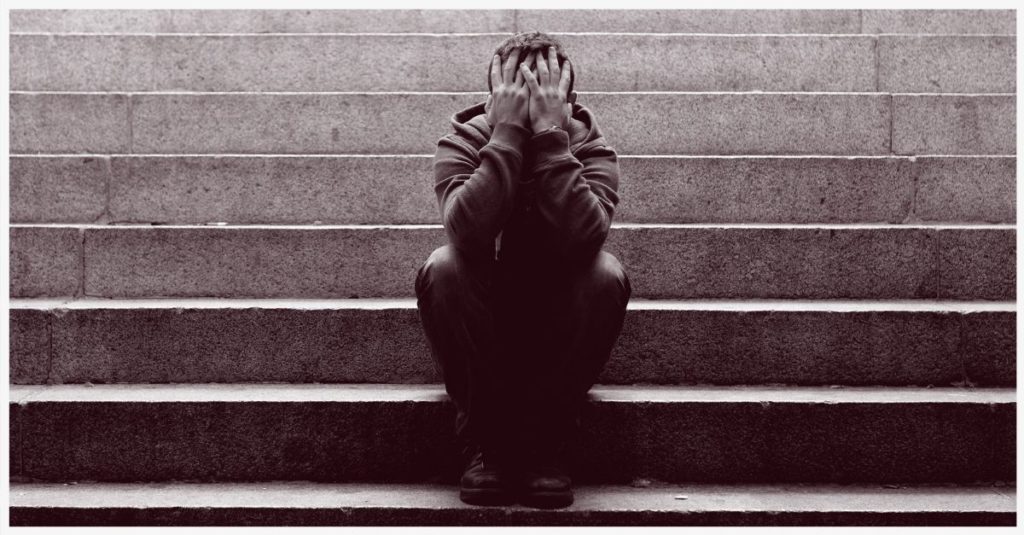 A man sitting on some steps covering his face while having a panic attack